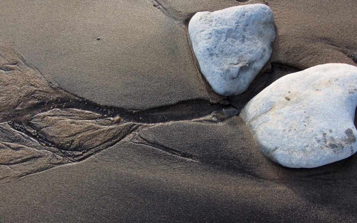a couple of rocks sitting on top of a sandy beach