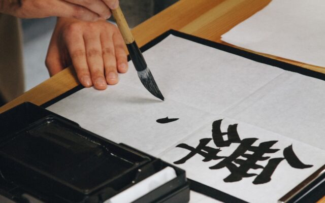 person holding black paint brush while painting black text on white paper