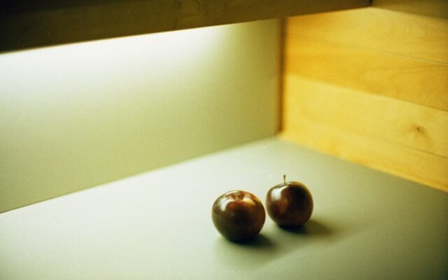 Two dark apples sit on a gray surface.