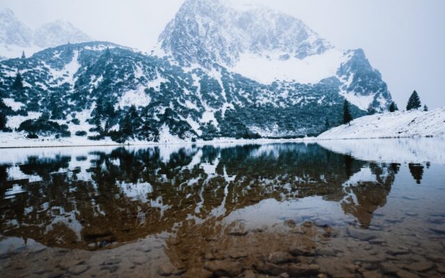Snow-covered mountains reflected in a calm lake.