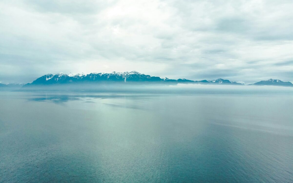 snow covered mountain beside ocean under white clouds