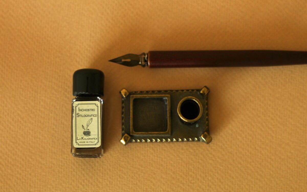 a pen, ink bottle, and a miniature camera on a table