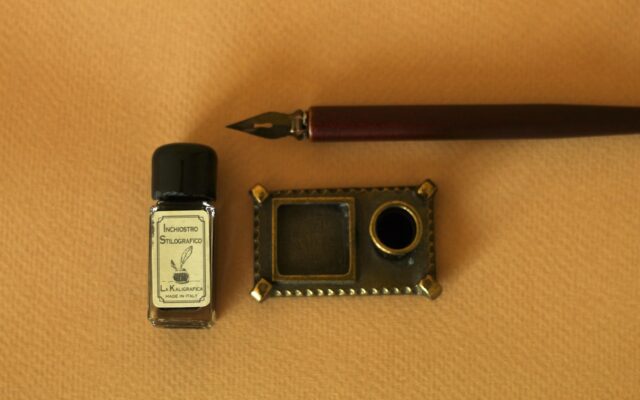 a pen, ink bottle, and a miniature camera on a table