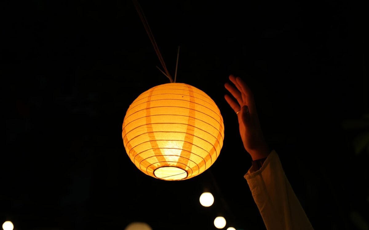 A hand reaches for a glowing paper lantern at night.