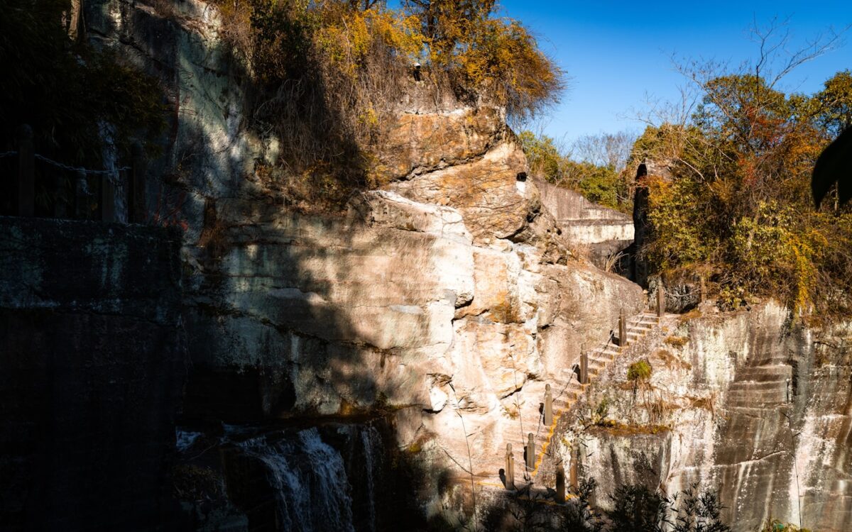 Stone stairs ascend a rocky cliff face with trees.