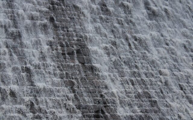 Water cascades down a textured stone dam face.