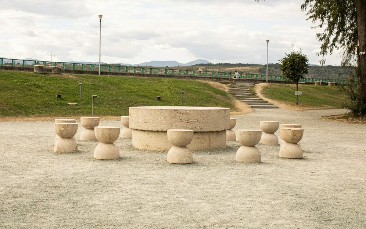 A circular stone table surrounded by hourglass shaped stone stools in a park